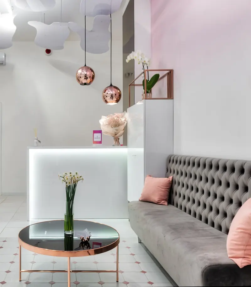 The front desk of a bright beauty studio, with a soft sofa and fresh flowers.